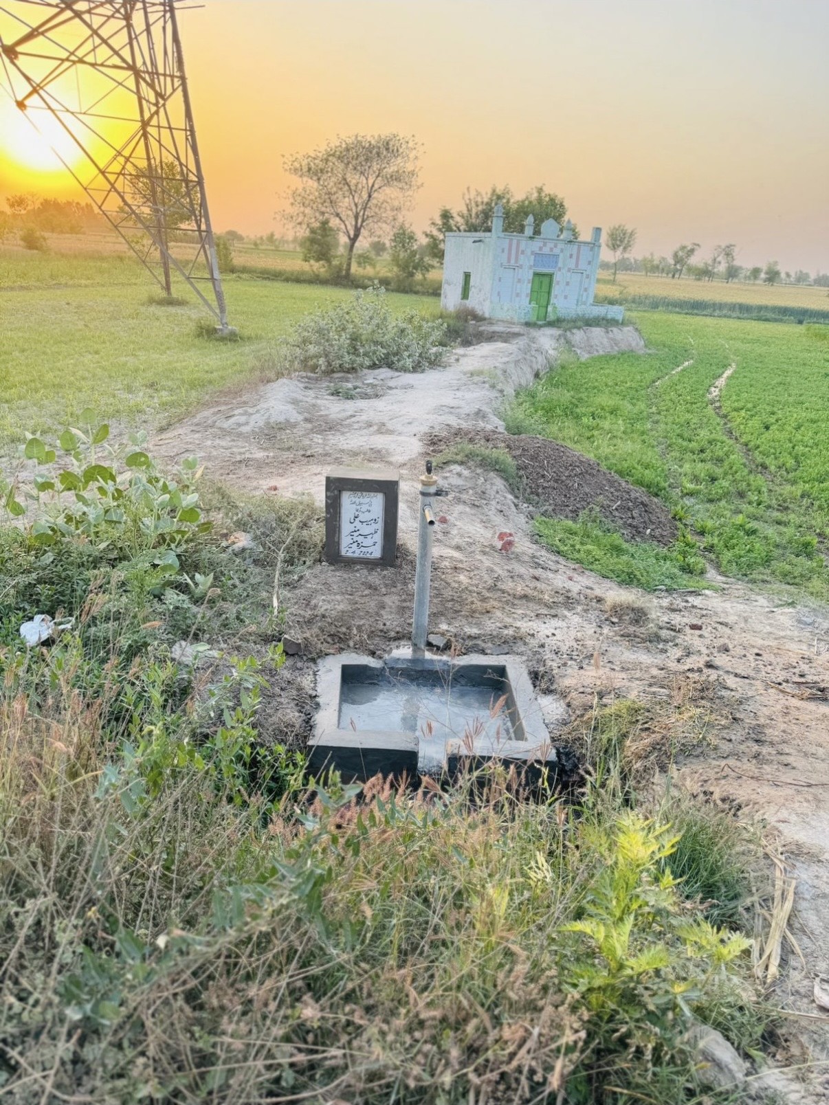 A completed hand-pump water point beside farmland at sunset