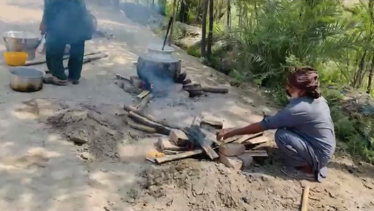 A community member tending a wood fire under a cooking pot