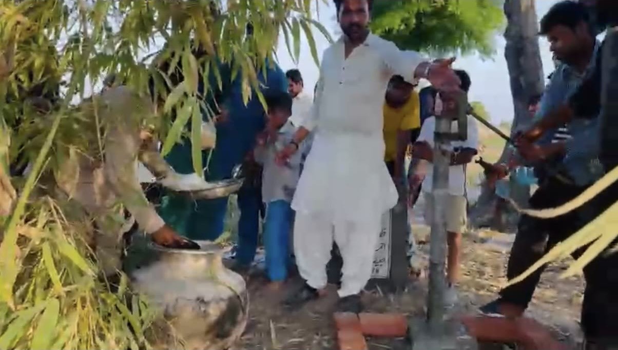 Community members gathered around a hand-pump water well under trees