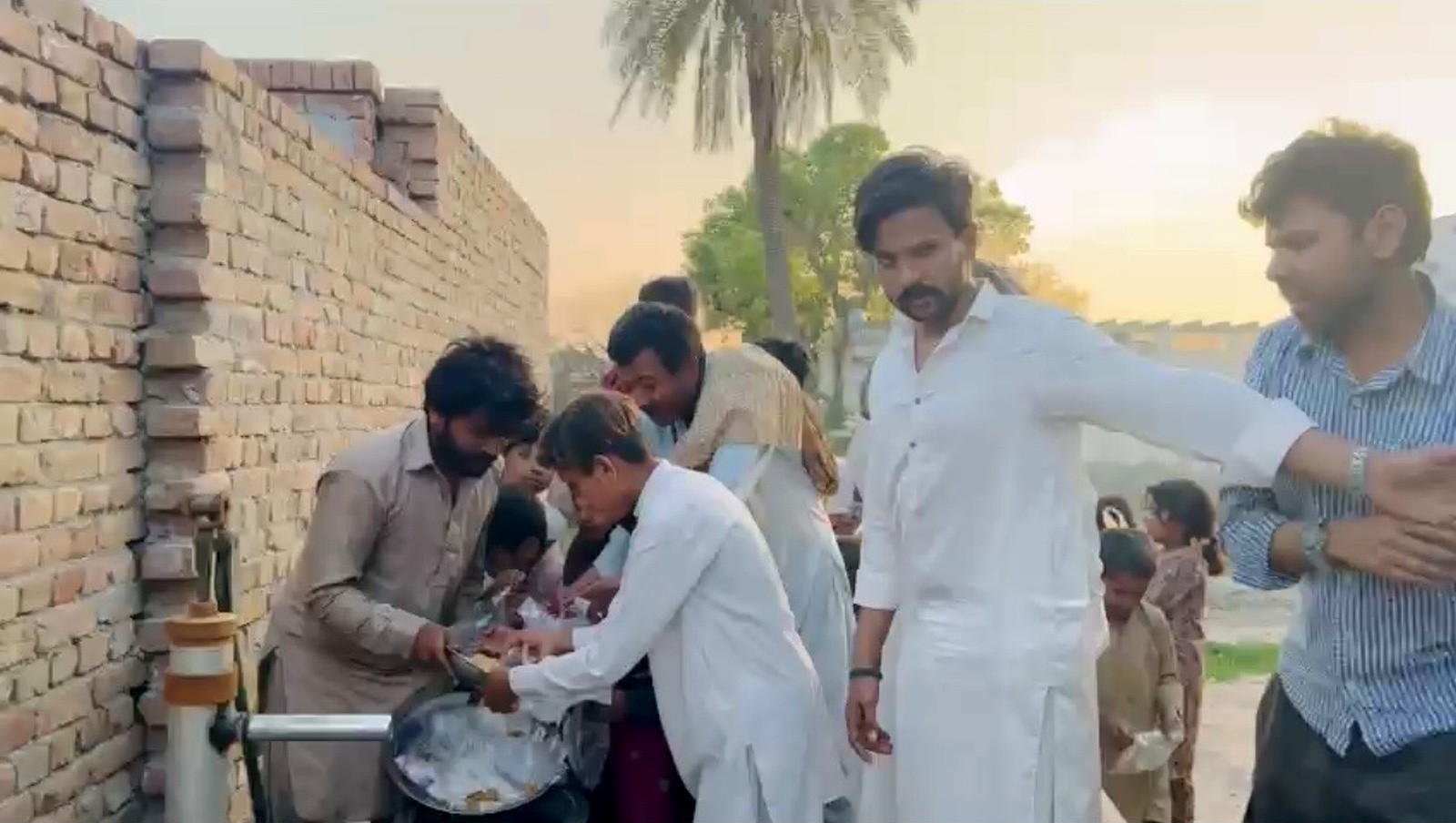 A group serving cooked food to children beside a brick wall