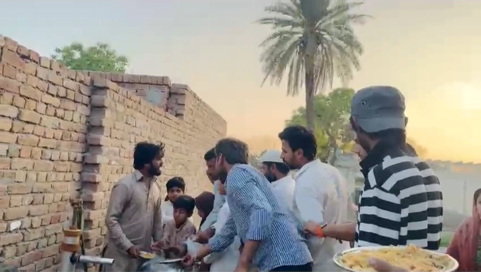 Community members serving plates of food in the evening light