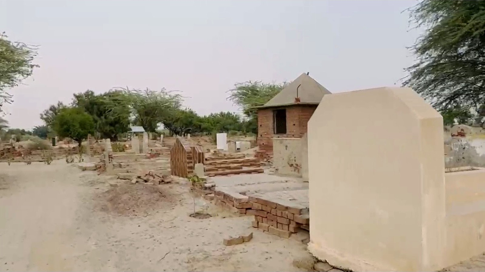 Open village grounds with trees and simple brick structures