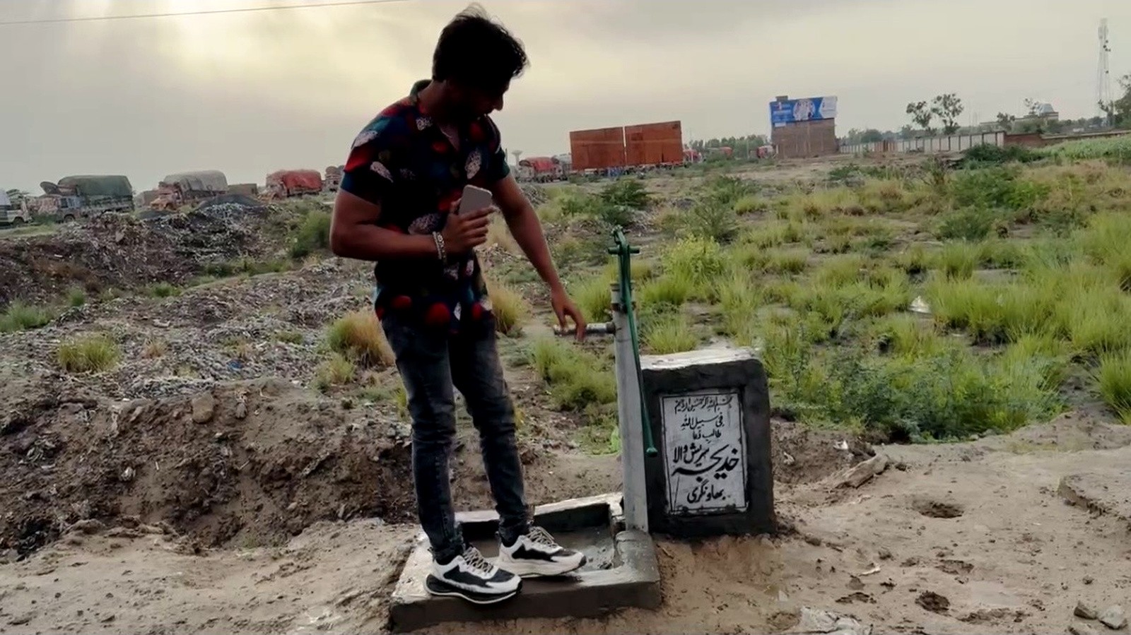 A young man checking a newly installed hand pump on open ground