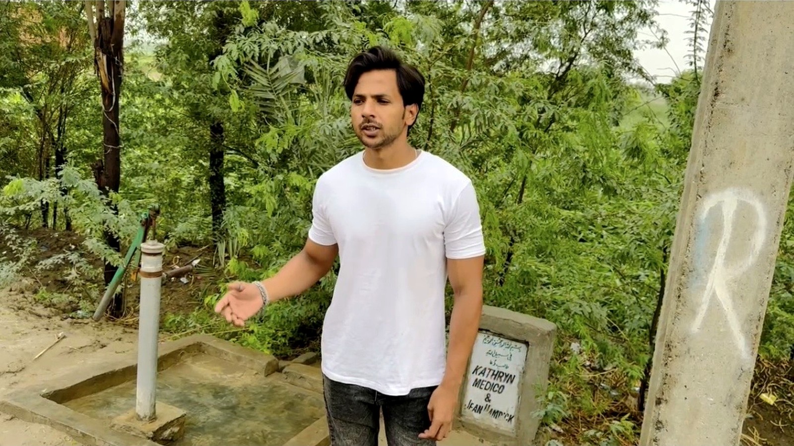 A man beside a completed hand-pump water point with a dedication plaque