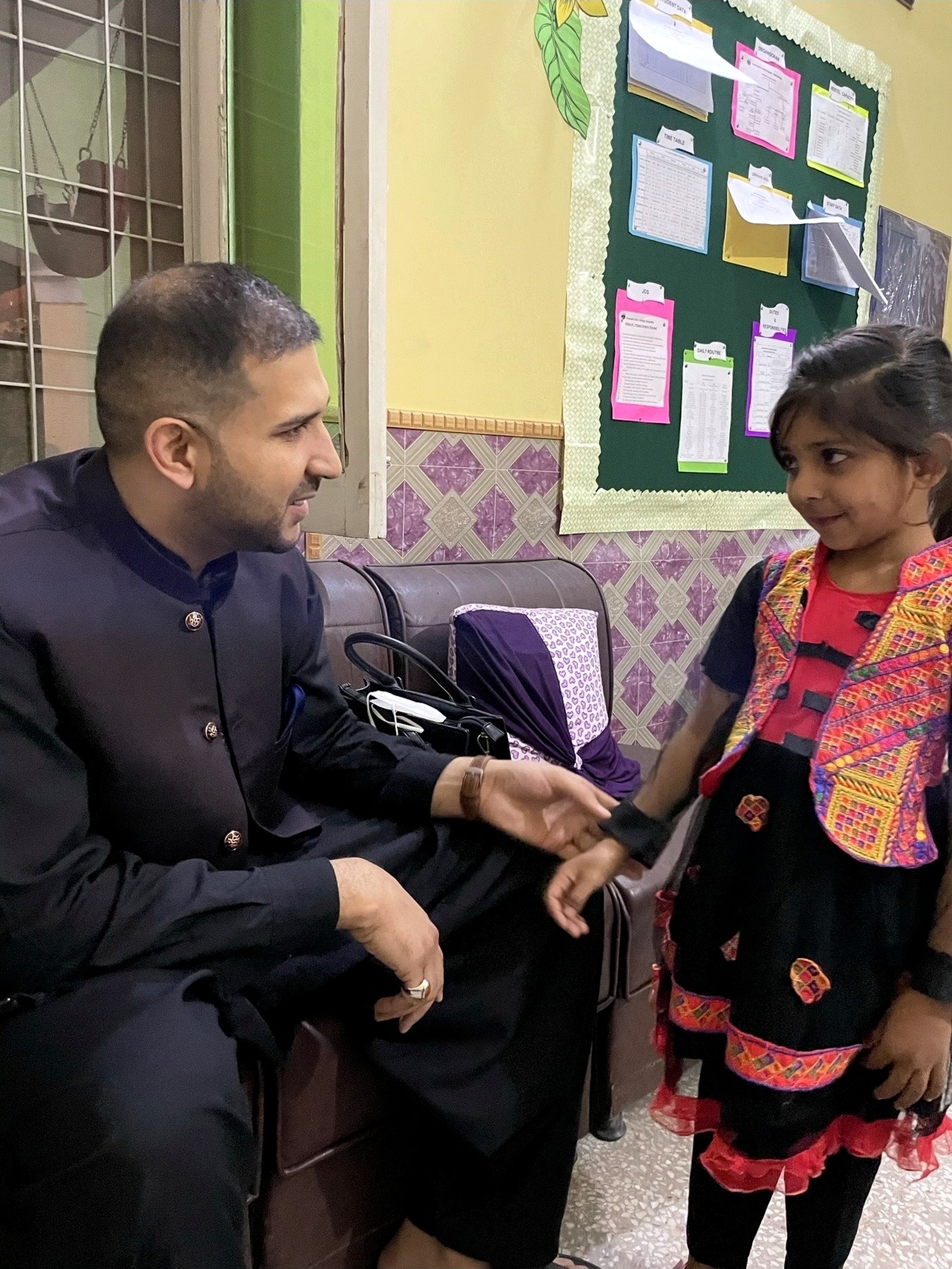 A man speaking with a young schoolgirl inside a classroom