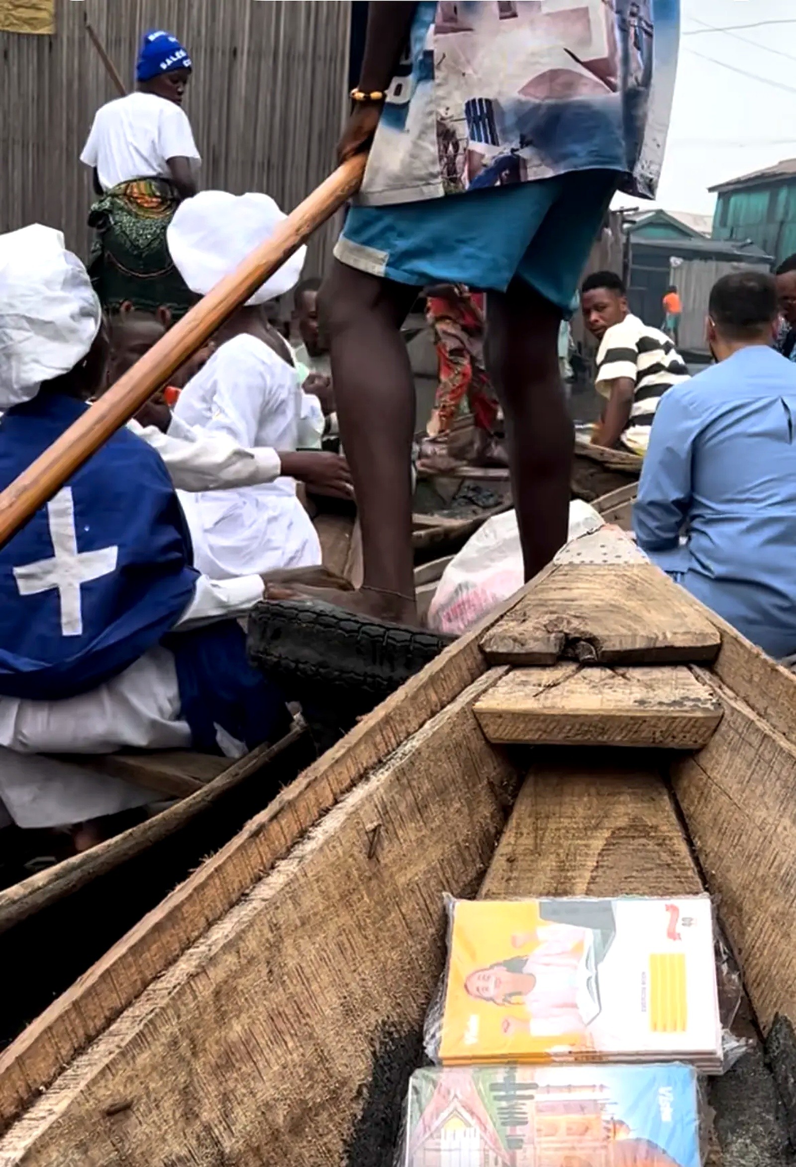 Packs of school exercise books in a wooden canoe among a waterside community