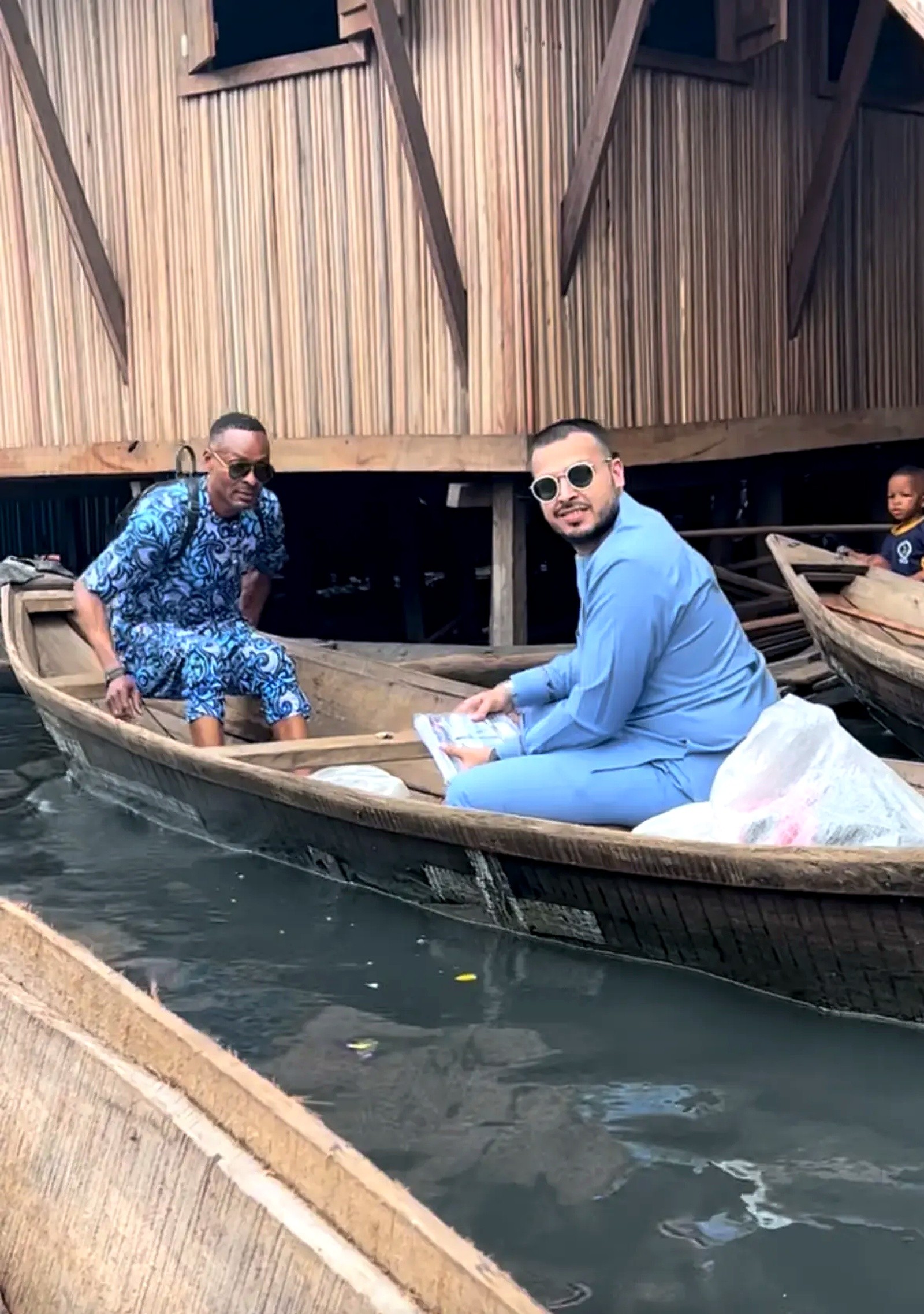 Two men seated in a wooden canoe beside stilt houses